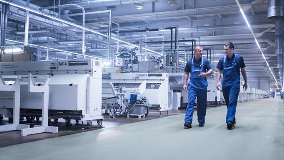 Eine Maschinenhalle mit zwei Mitarbeitern die zur Kamera laufen und sich unterhalten