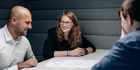 zwei männliche und eine weibliche Häring-Mitarbeiterin sitzen in einer Besprechung lachend am Tisch